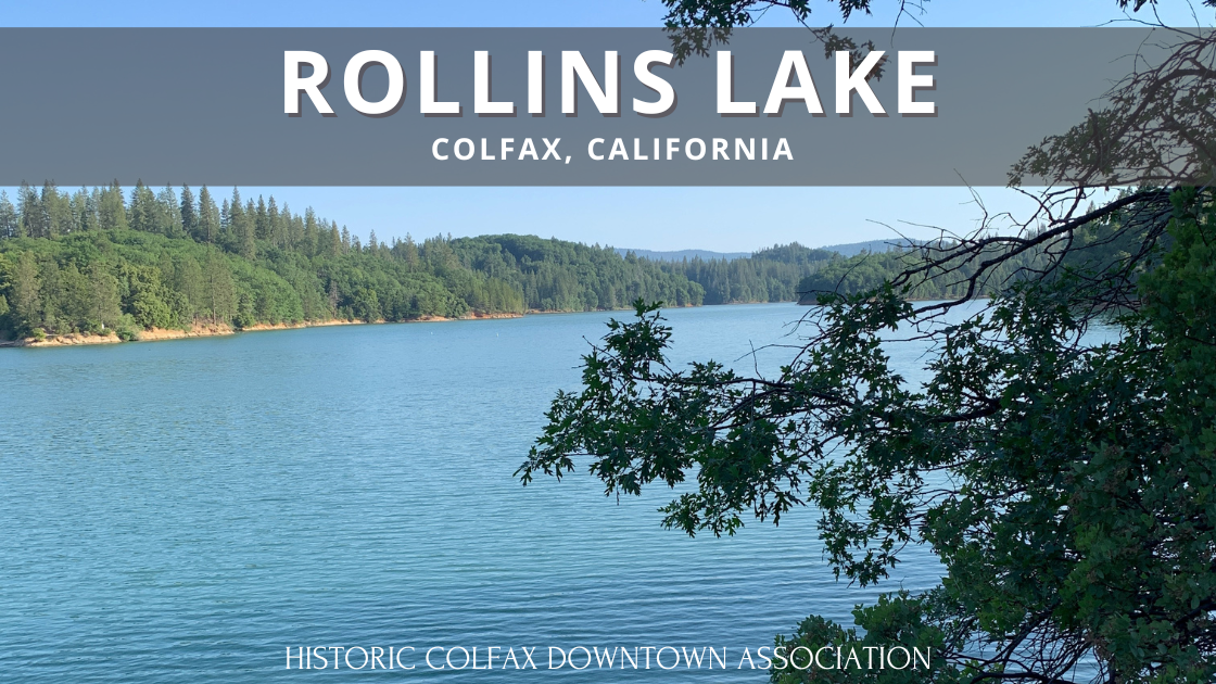 A scenic view of Rollins Lake in Colfax, CA, with calm waters, lush greenery, and blue skies.